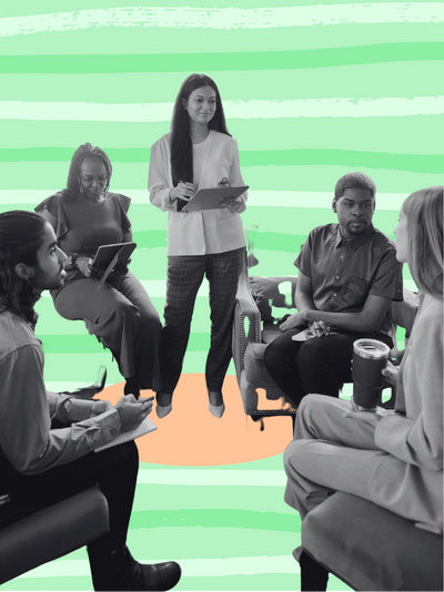 A black and white image of a group of multi-racial and multi-generational people sitting in a circle, holding coffee and notepads and talking with each other.