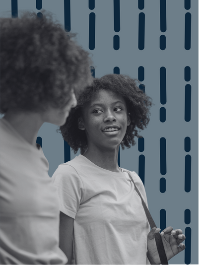 A black and white image of two women with afros standing and smiling as they look at each other.